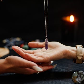 Side view closeup of fortune teller holding magic crystal over palm of young woman and reading her destiny in spiritual seance