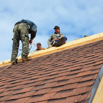 KYIV, UKRAINE - February, 05, 2018: Roofer laying asphalt shingles. Roofer with safety kit on the house roof installing, repair asphalt shingles.Roofing construction. Roofer's Kits for Fall Protection