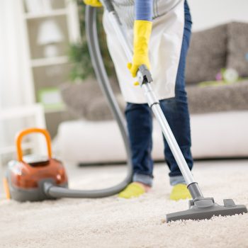 Housewife from cleaning service cleans carpet with vacuum cleaner