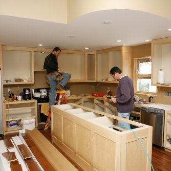 Cabinet maker installing custom made kitchen island and cabinets, while electrician installs in-cabinet lighting.Very shallow DOF quickly drops off to nice soft focus.