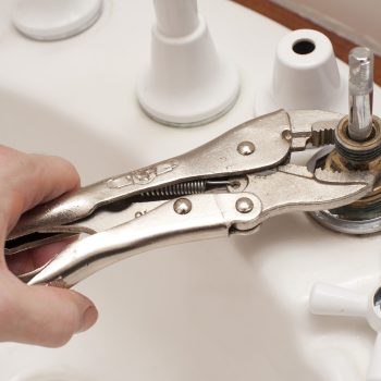 Man repairing a broken faucet or tap on a bathroom sink using a mole grip pliers in a DIY and renovation concept