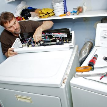Homeowner repairman bends over to inspect the wiring and fuses to fix the non-heating gas dryer