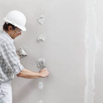 man drywall worker or plasterer putting plaster on plasterboard wall using a trowel and a spatula, fill the screw holes, wearing white hardhat and safety glasses.