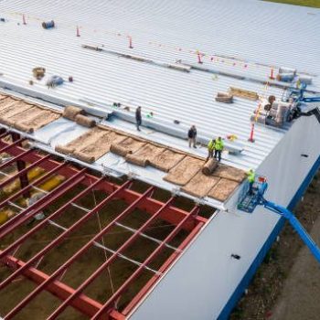 Milwaukee, WI, USA - September 15, 2020: Construction workers installing insulation and roof panels on a large warehouse building.