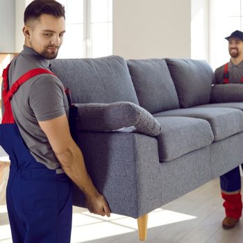 Two,Professional,Relocation,Service,Workers,In,Overalls,Move,Sofa,In
